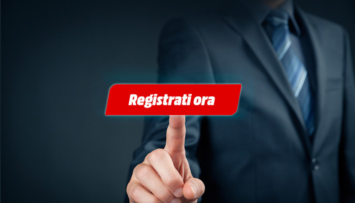 Uomo in giacca e cravatta che tocca un pulsante rosso con la scritta "Registrati ora" su sfondo scuro.