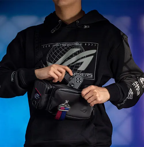 Uomo con felpa nera con logo, che infila controller nero in una borsa a tracolla nera. Sfondo blu sfumato.