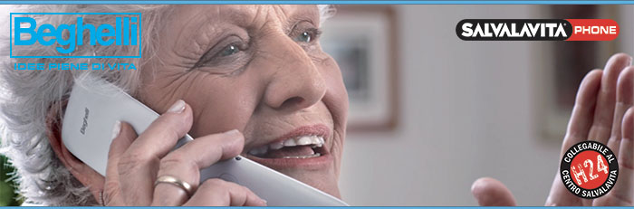 Pubblicità di Beghelli Salvavita Phone. Donna anziana usa telefono bianco. Logo prodotto in evidenza.