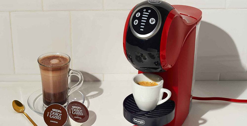 Macchina da caff� rossa con tazza bianca, bevanda al cioccolato in vetro e capsule su un tavolo bianco.