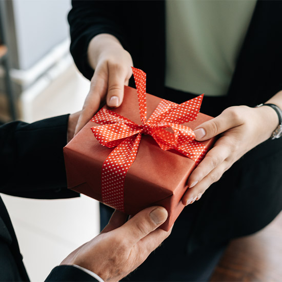 Due persone si scambiano un regalo rosso con un fiocco a pois bianchi. Le mani tengono il pacchetto.