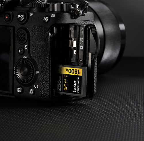 Fotocamera nera con scheda di memoria Lexar inserita nello slot, su sfondo nero testurizzato.