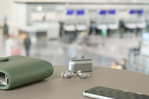 Portafoglio verde, auricolari senza fili e smartphone su un tavolo. Sullo sfondo, un'area sfocata con sedili blu.