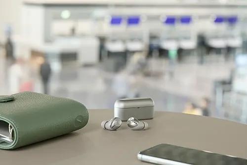 Portafoglio verde, auricolari senza fili e smartphone su un tavolo. Sullo sfondo, un'area sfocata con sedili blu.
