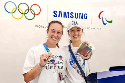 Due donne sorridenti con magliette bianche e medaglie, sullo sfondo loghi olimpici e Samsung.