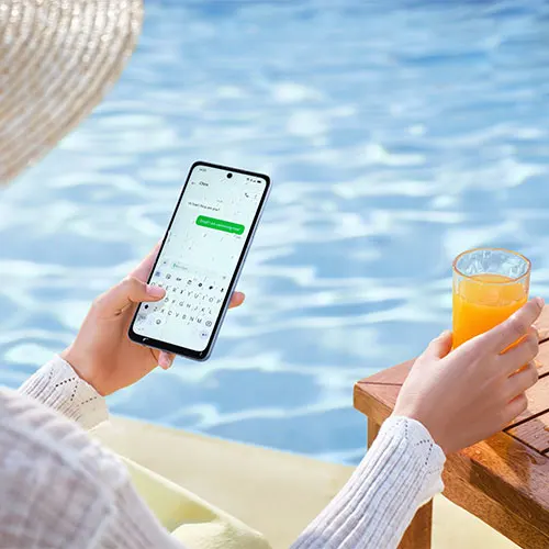 Persona con telefono e succo su tavolo di legno, piscina sullo sfondo.