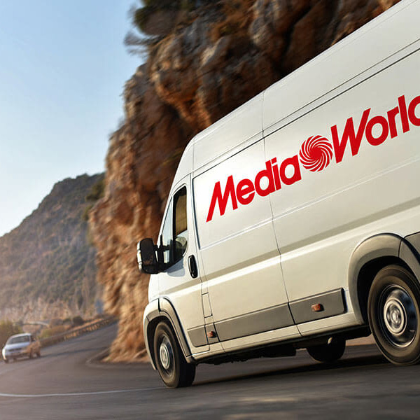 Furgone bianco "Media World" su strada asfaltata, sfondo montuoso e cielo azzurro. Altra auto visibile in lontananza.