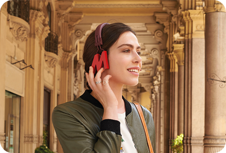 Donna con cuffie rosse a forma di "M", giacca verde, sullo sfondo architettura classica.