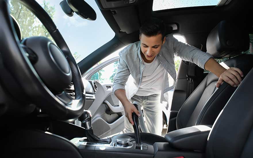 A young man precisely vacuums his car’s interior, paying close attention to the front seats and dashboard area for cleanliness.
