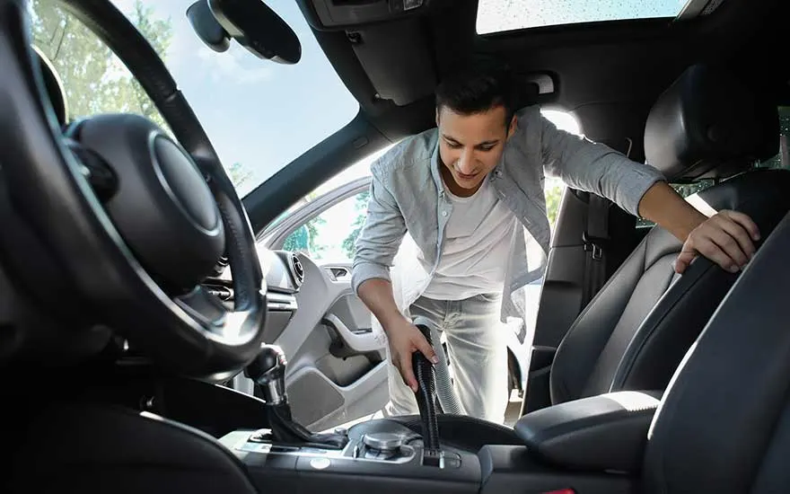 A young man precisely vacuums his car’s interior, paying close attention to the front seats and dashboard area for cleanliness.
