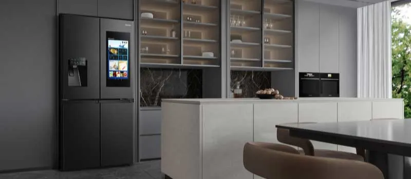 Een moderne keuken met zwarte slimme koelkast, groot eiland, open kasten, ingebouwde oven en eettafel in een strak grijs interieur.