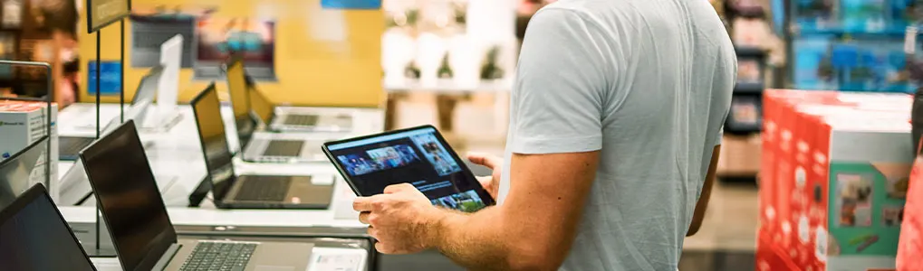 Man bekijkt een tablet in een winkel, met laptops op een rij op de voorgrond.