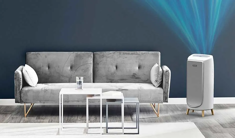 Grijze fluwelen bank met witte salontafels en een luchtreiniger die blauwe lucht projecteert tegen een donkere muur.