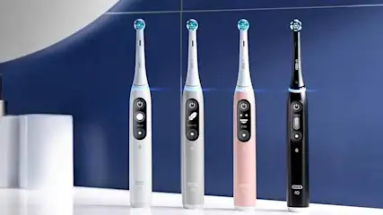 Vier Oral-B iO Series 6 elektrische tandenborstels staan rechtop op une witte plank tegen een blauwe achtergrond, strak en modern.