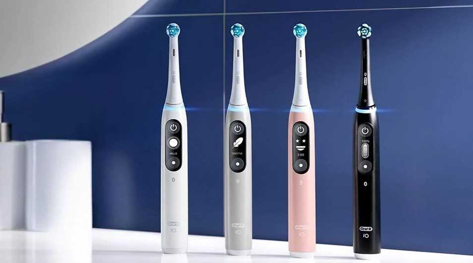 Four Oral-B iO Series 6 electric toothbrushes stand upright on a glossy white surface before a blue wall, sleek and futuristic.