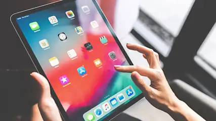 Een persoon gebruikt een tablet met een kleurenscherm vol app-pictogrammen, inclusief een dock met Safari en Mail.