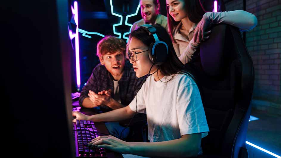 Een vrouw met een koptelefoon en bril typt op een toetsenbord, omringd door drie kijkende mensen in een donkere kamer met neonlicht.