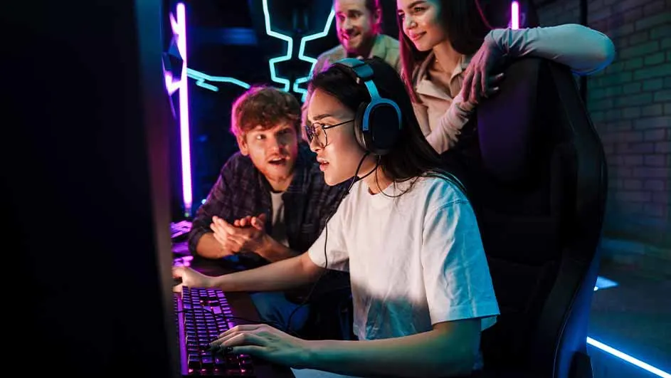 Een vrouw met een koptelefoon en bril typt op een toetsenbord, omringd door drie kijkende mensen in een donkere kamer met neonlicht.