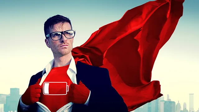 Man met bril en rode cape op een rood shirt met een batterij-icoon, tegen een achtergrond van een stadsgezicht.