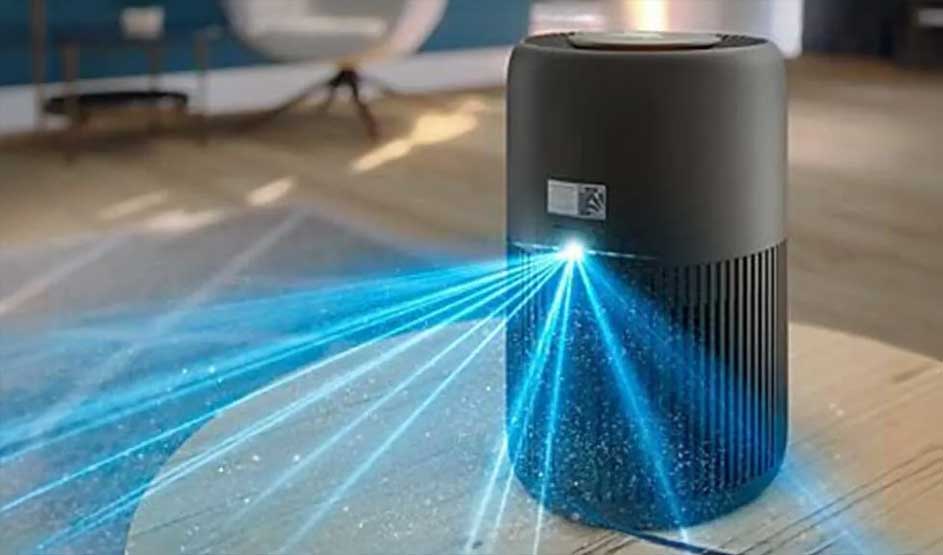 Black air purifier on a table projects bright blue beams across the floor, visually showing purified, cleaner room air spreading around.