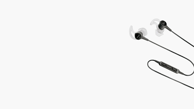 Zwarte oortelefoons met bedieningselementen en witte siliconen oordopjes liggen op een witte achtergrond.