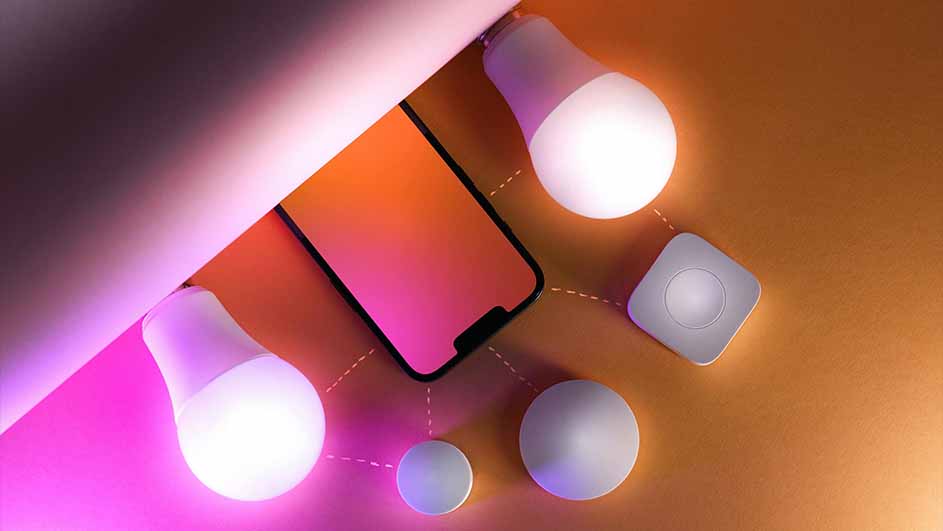 Een smartphone met oranje scherm, twee gloeilampen, een vierkante afstandsbediening en een ronde knop op een oranje achtergrond.