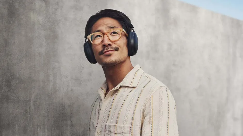 Man draagt een gestreept overhemd, een bril en een koptelefoon tegen een grijze achtergrond.