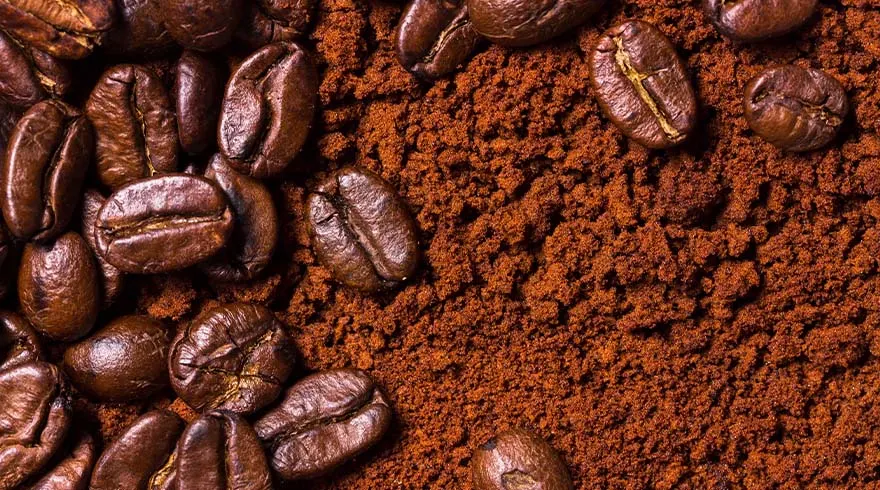 Bruine koffiebonen liggen op gemalen koffie. De bonen zijn heel en hebben een ovale vorm.