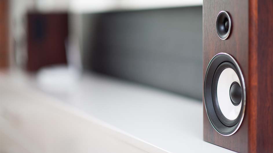 Een bruine houten luidspreker met twee ronde luidsprekers staat op een wit oppervlak met een grijze achtergrond.