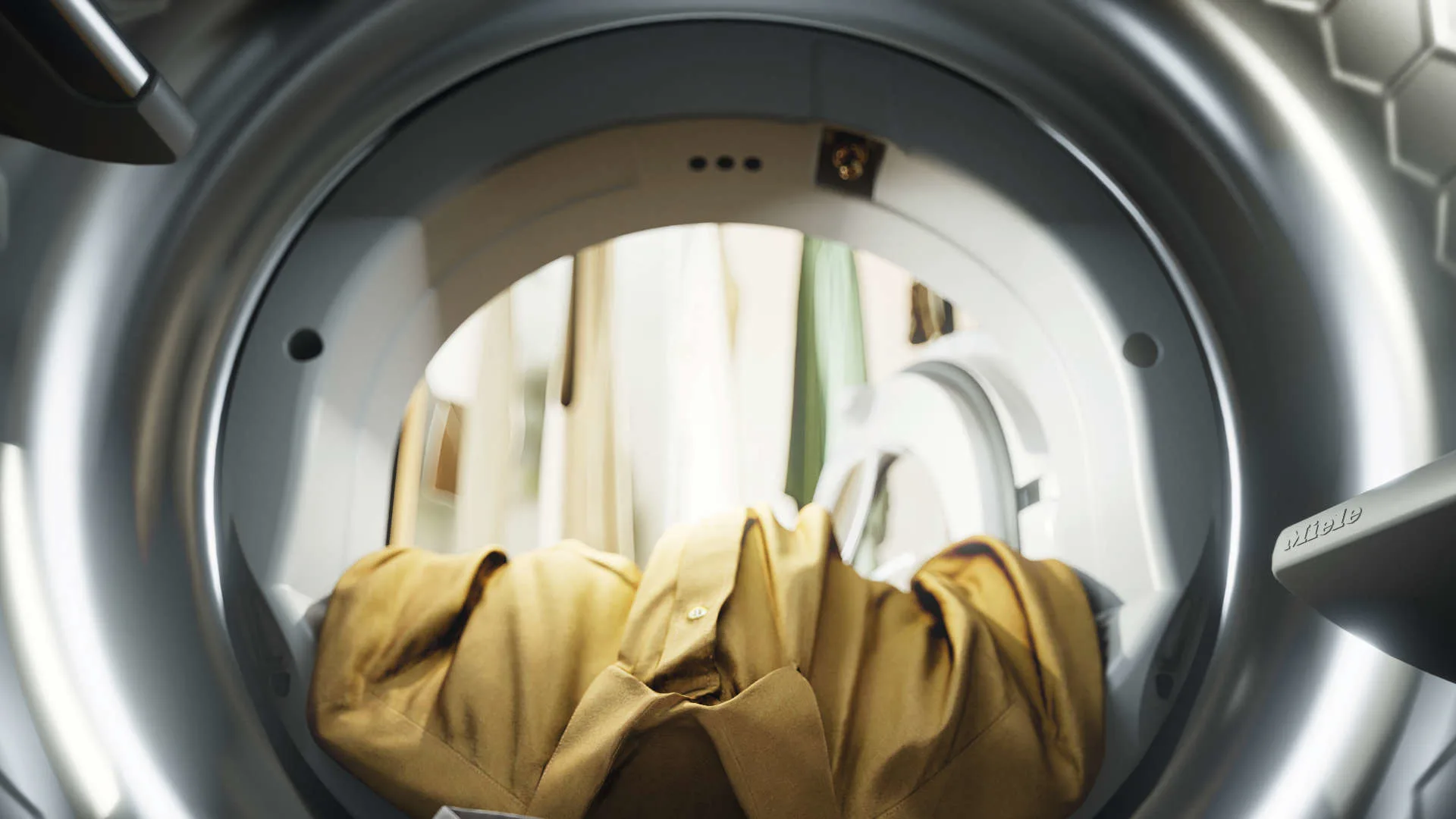 Gouden overhemden liggen in een zilverkleurige wasmachine met een witte achterwand.