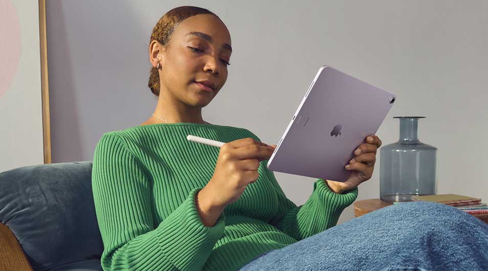 Vrouw ontspant op een bank en gebruikt een paarse tablet met stylus, geconcentreerd schrijvend of tekenend in een rustige woonkamer.
