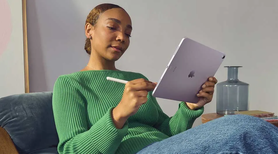 Vrouw ontspant op een bank en gebruikt een paarse tablet met stylus, geconcentreerd schrijvend of tekenend in een rustige woonkamer.