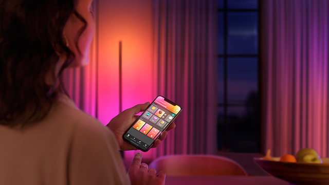 Een vrouw houdt een smartphone vast met een app in een roze kamer met een raam met gordijnen.