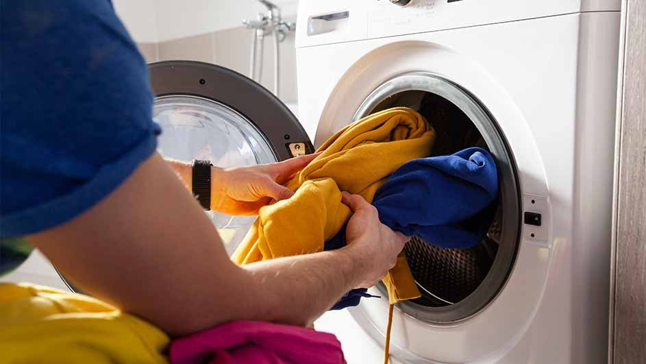 Person loads blue and yellow clothes into a white washing machine with a dark gray door frame.