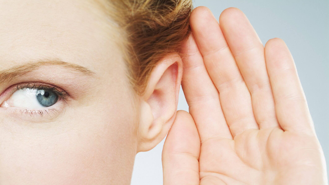 Een close-up van een persoon die een hand aan het oor houdt tegen een blauwe achtergrond.