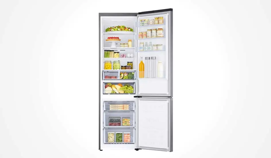 Een zilveren koelkast met ondervriesvak staat open, gevuld met groenten, fruit, flessen, potjes en diepvriesproducten. Alles is netjes ingedeeld.