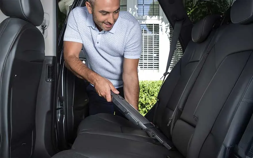 Een man reinigt zorgvuldig de achterbank van zijn auto met een stofzuiger om vuil en stof te verwijderen en de bekleding netjes te houden.