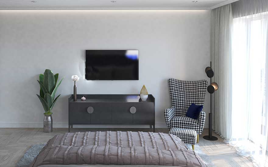 In a bright bedroom, a TV is mounted on the wall across from the bed, with an armchair, plants, and cabinet nearby.