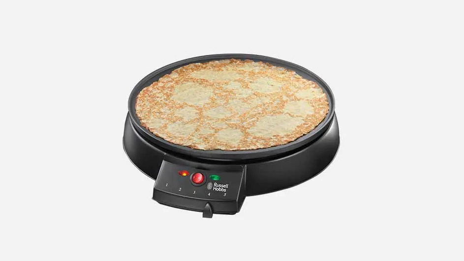 Een pannenkoekenmaker met een gebakken pannenkoek erop, tegen een witte achtergrond. Het apparaat is zwart met een bedieningspaneel.
