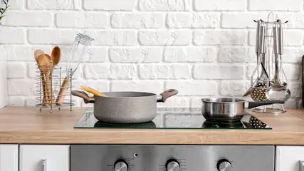 Een keuken met witte bakstenen achterwand, houten aanrechtblad, pannen op een kookplaat en keukengerei.
