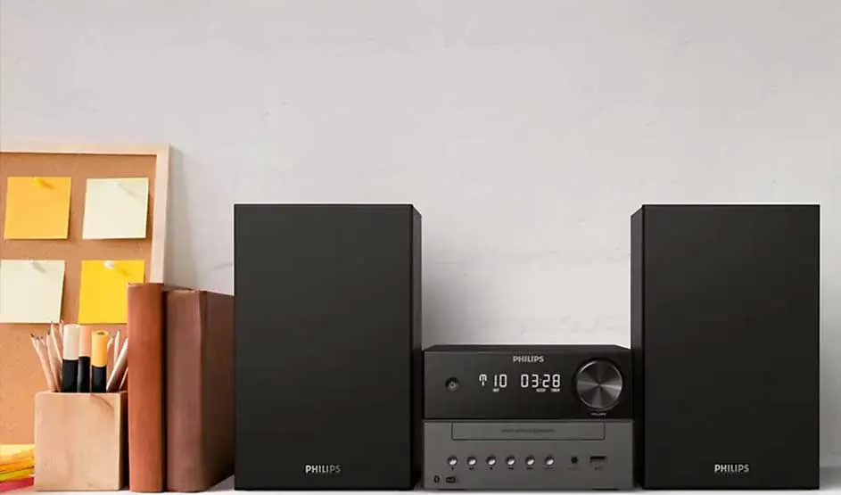 Een Philips stereoset met twee zwarte speakers staat op een bureau naast boeken, pennen en een prikbord met gele notities.