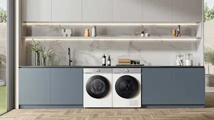 Moderne keuken met blauwe kasten, marmeren achterwand en centraal ingebouwde witte wasmachine en droger naast elkaar.