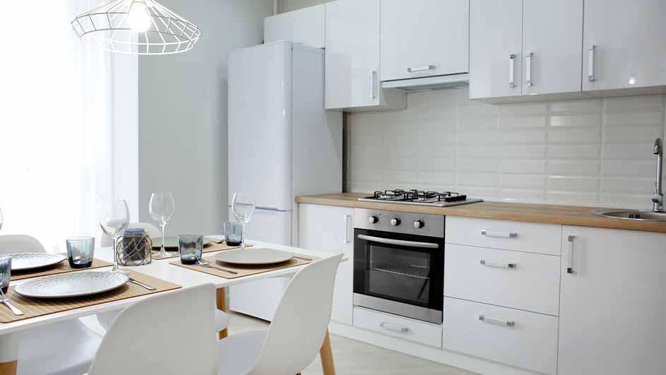 Een moderne keuken met witte kasten, een roestvrijstalen oven en een tafel met gedekte borden en glazen.