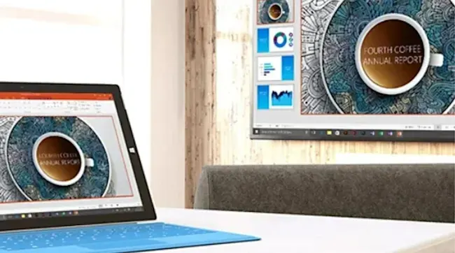 Een blauwe laptop en een scherm tonen een jaarverslag met een koffiekop op een witte tafel tegen een houten achtergrond.