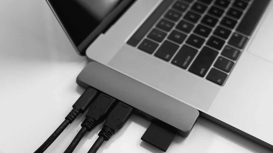 Een grijze laptop met een hub eraan bevestigd, met zwarte kabels en een kaart die in de hub zijn gestoken.