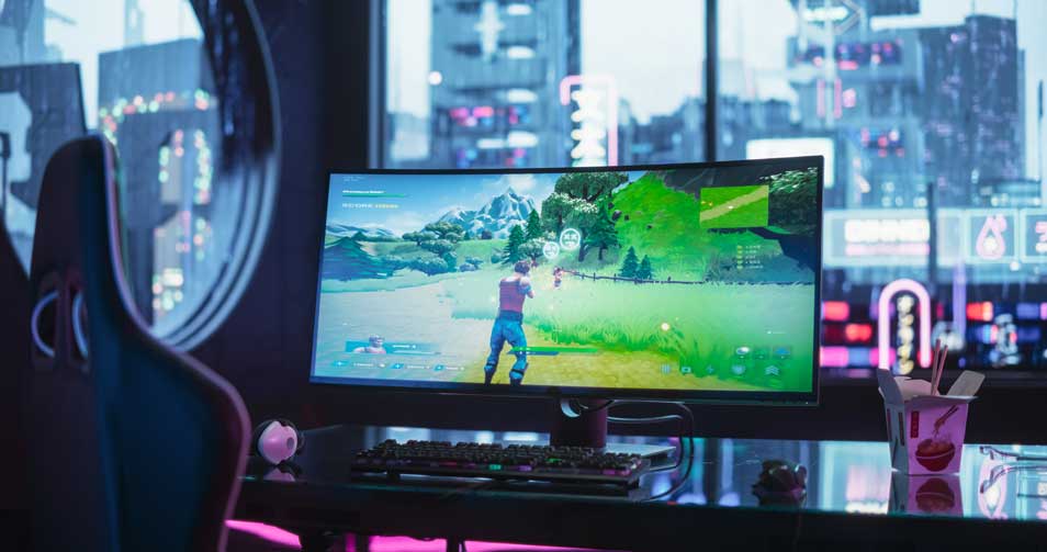 Ultra-wide gaming monitor showing shooter, neon-lit desk with keyboard, mouse and takeaway box in front of a city view.