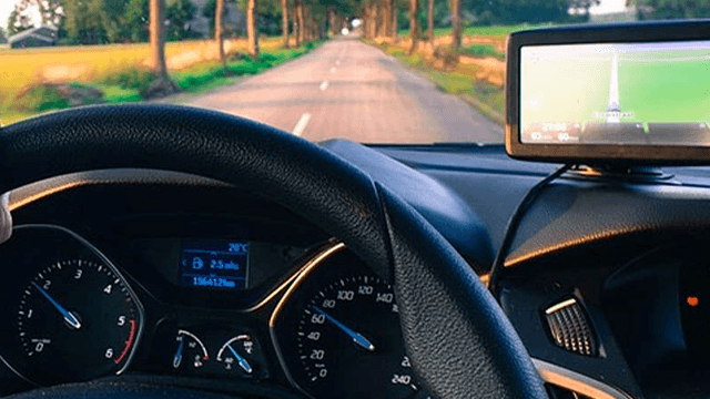 Uitzicht vanuit een auto met een navigatiesysteem en een weg met bomen aan beide kanten.
