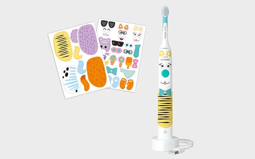 Een kindertandenborstel met kattengezicht en gele strepen staat naast kleurrijke stickers op een eenvoudige witte achtergrond.