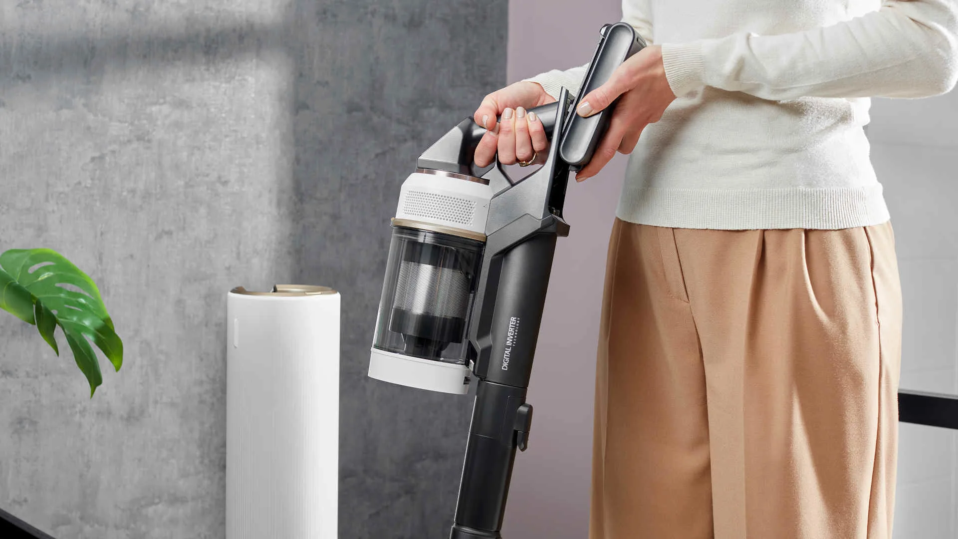 Een persoon houdt een zwarte en witte stofzuiger vast in een kamer met een grijze muur en een witte luchtzuiveraar.