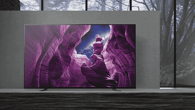 Een tv toont een paarse canyon met een blauwe lucht, geplaatst voor een raam met bomen.